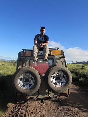 Student sits on top of jeep in African bush.