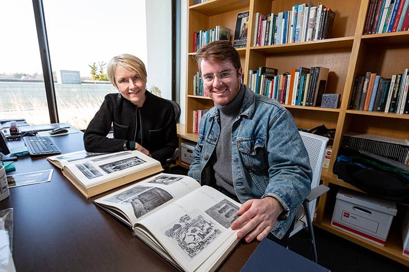 Professor and student examine art history volume in book-lined office
