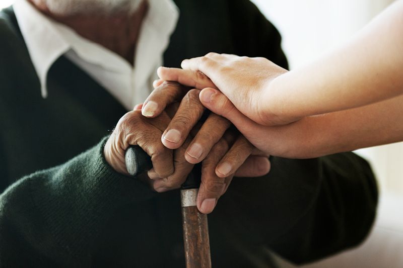 young hands resting on old hands resting on cane