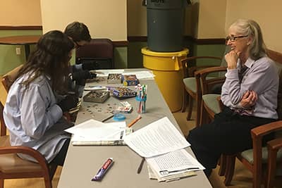 professor chats with students doing a puzzle with goggles and gloves on.