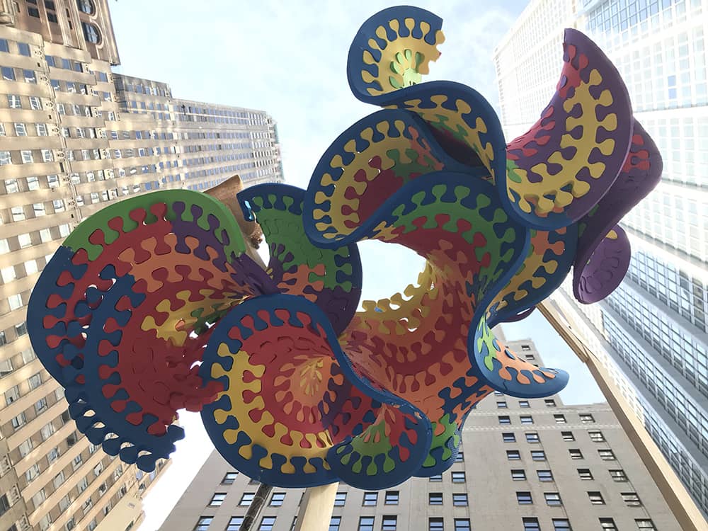 Multicolored lettuce-like form is suspended between skyscrapers