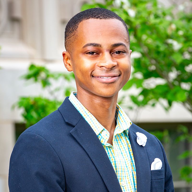 Young man in suit poses in front of Collegiate-Gothic-style building.