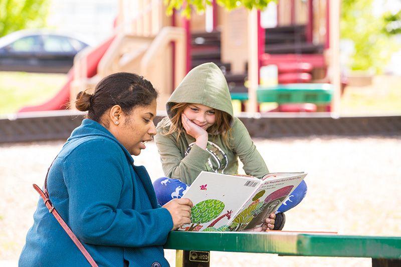 Student is reading to a school child on a playground.