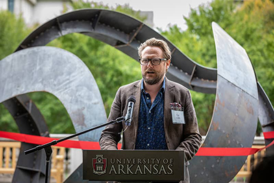 Professor speaks in front of a curved steel sculpture