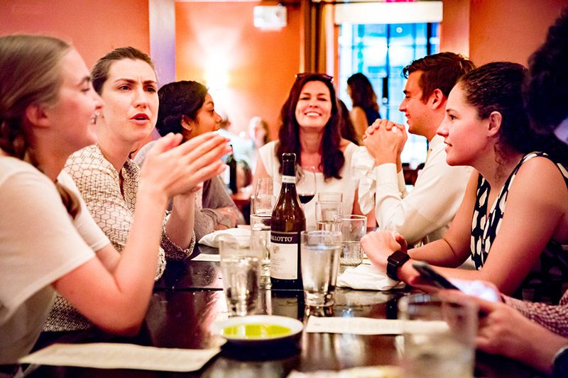 Female professor at head of table with students talking animatedly.