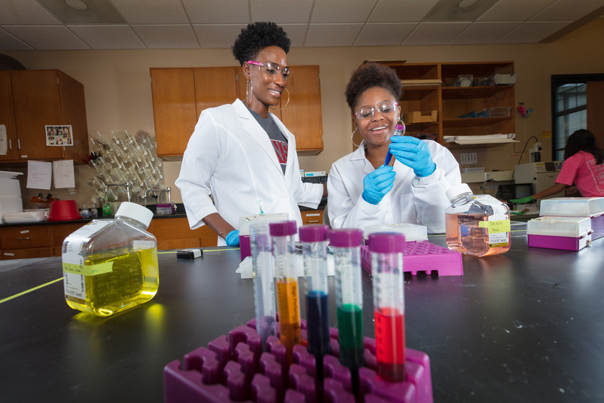 Young woman handles test tube while mentor looks on.