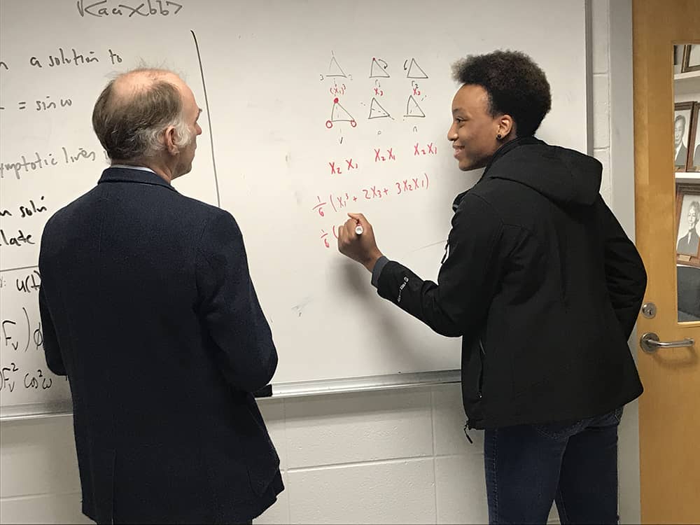 Female student and male professor work on a math problem on a white board. 