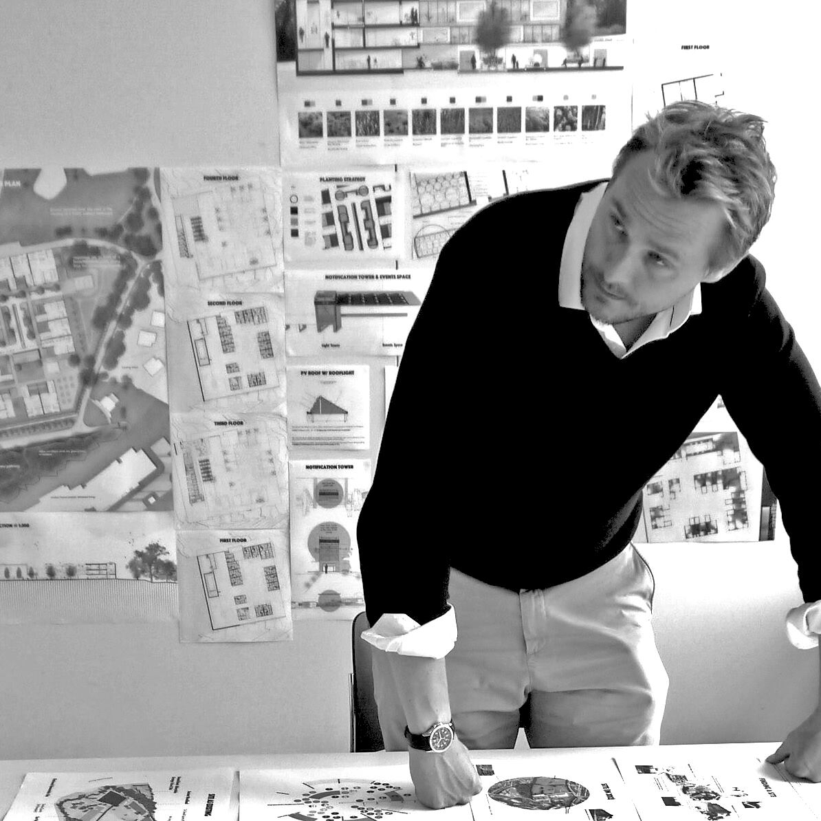 black and white of man leaning on desk strewn with papers