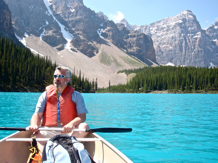 man sits in canoe beneath mountains