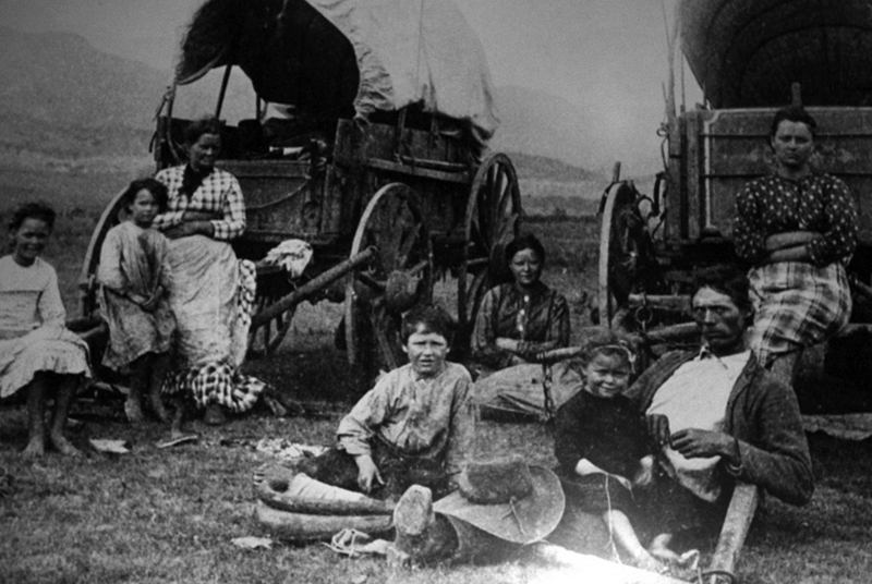 Frontier family poses in front of covered wagon; photo.