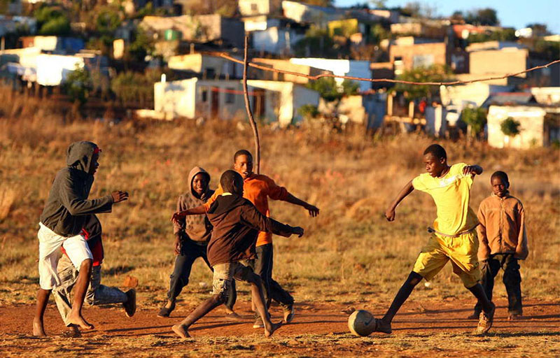 Children playing soccer in a brown field 